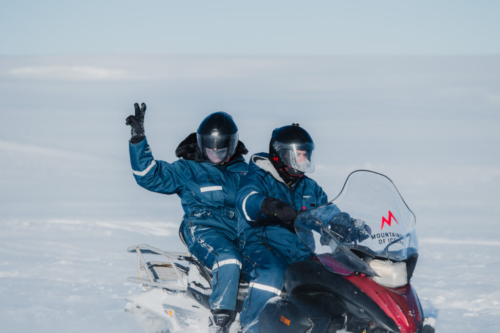 Two people on a snowmobile. One person is holding up a peace sign.