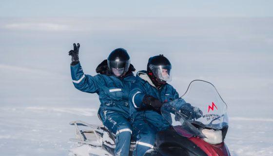 Two people on a snowmobile. One person is holding up a peace sign.